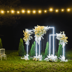 Wedding arch with lights and chairs outdoors.